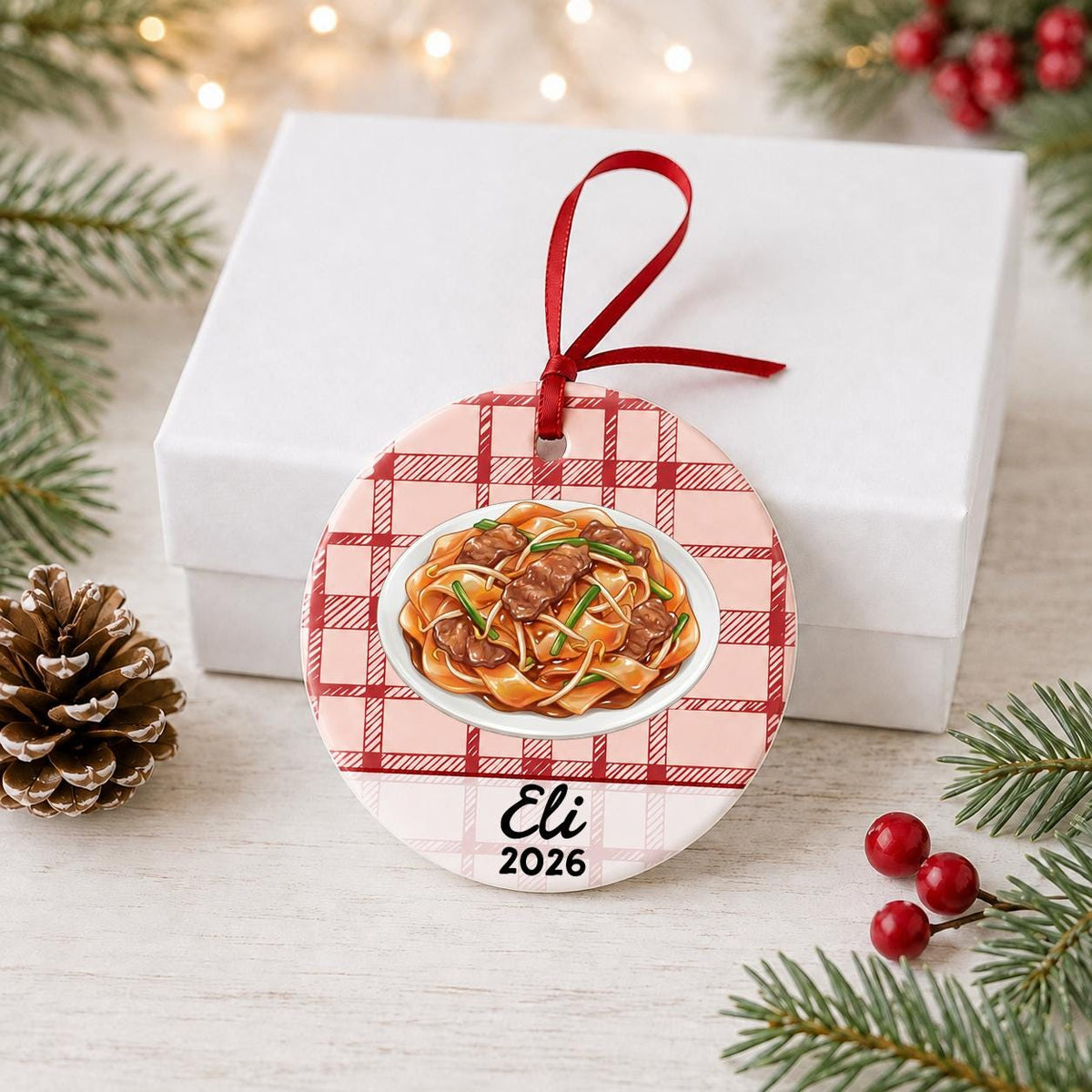 Personalized beef chow fun ceramic ornament with name and year on red plaid in front of a white gift box with pinecones and red berries