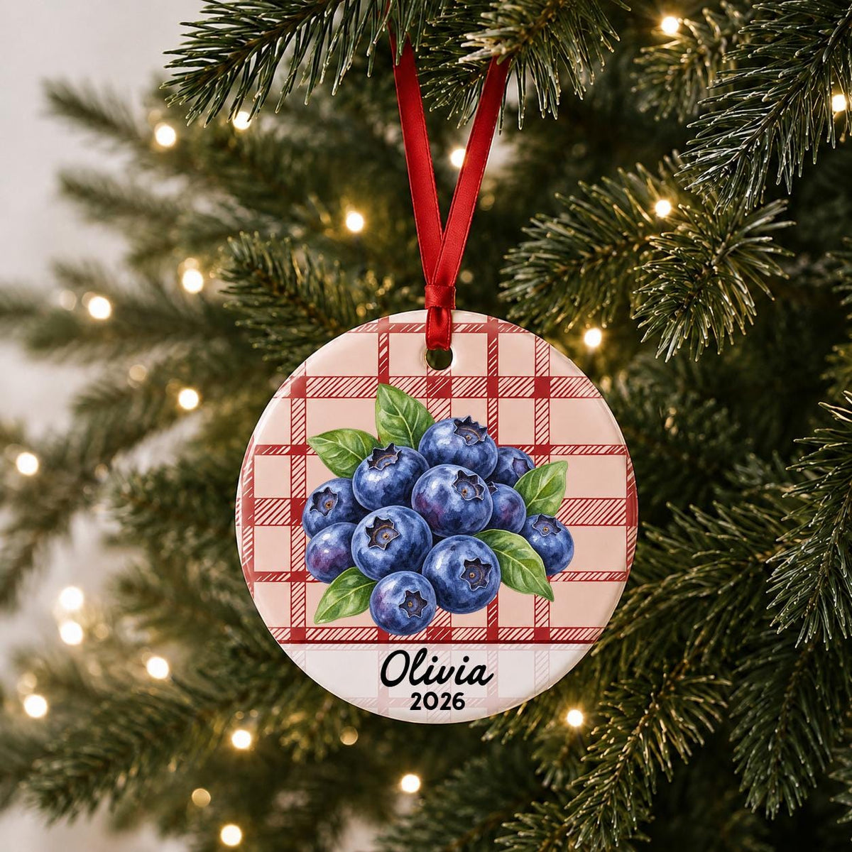 Personalized blueberries ceramic ornament with name and year on red plaid hanging on a lit Christmas tree