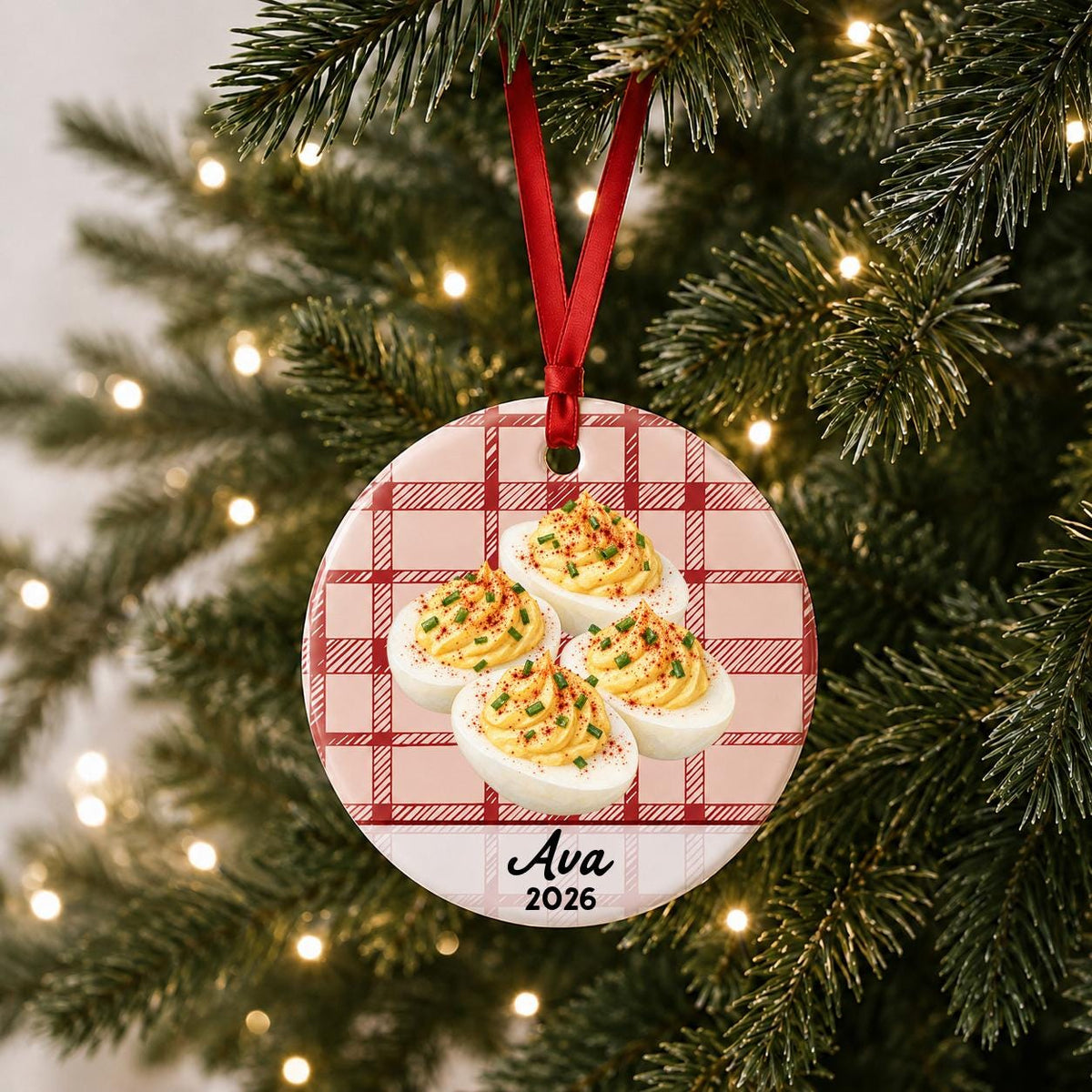 Personalized deviled eggs ceramic ornament with name and year on red plaid hanging on a lit Christmas tree