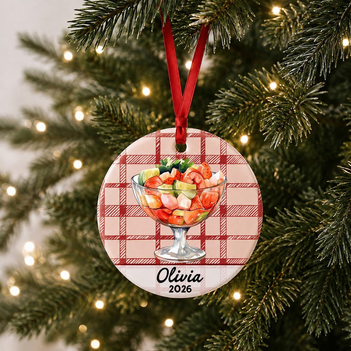 Personalized shrimp cocktail ceramic ornament with name and year on red plaid hanging on a lit Christmas tree