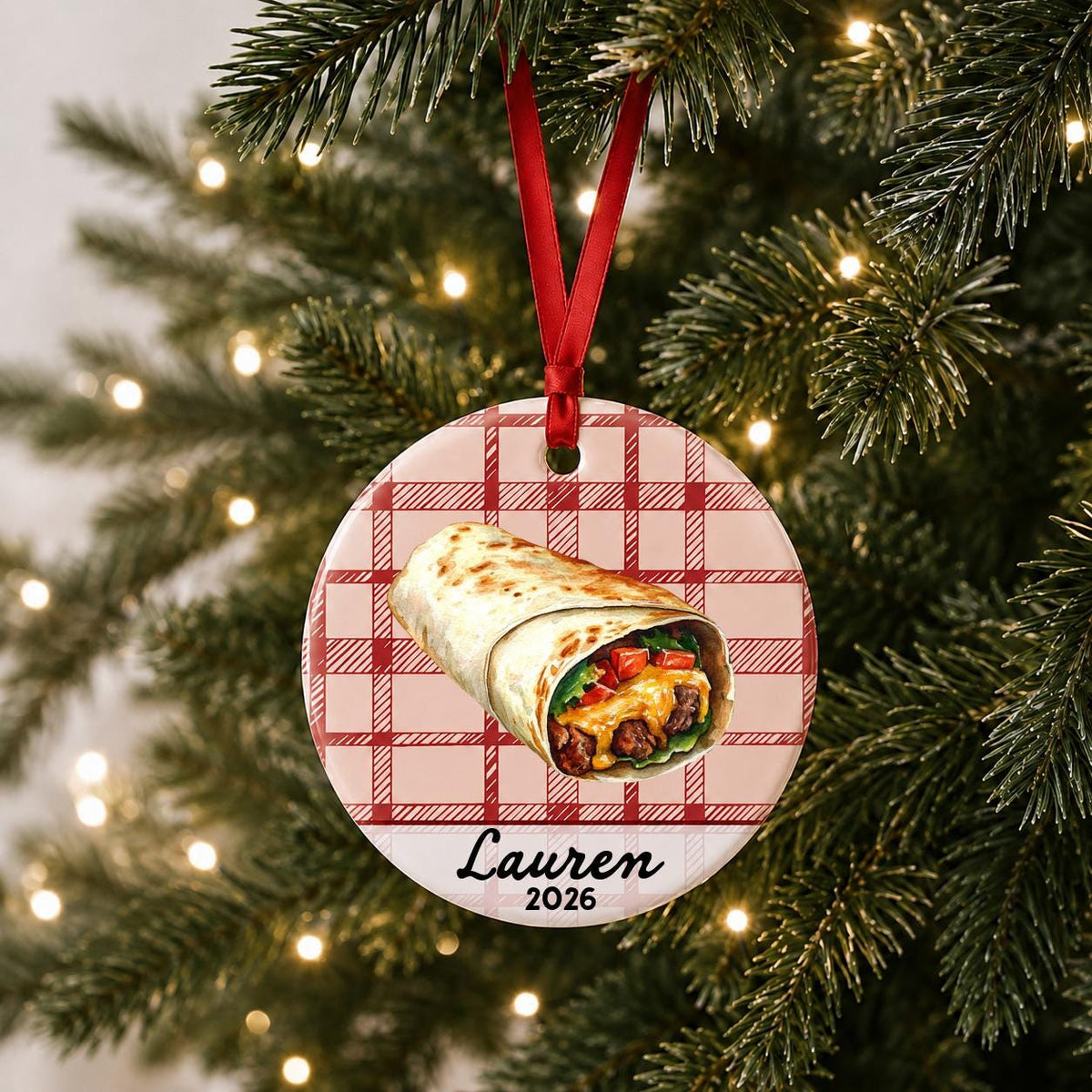 Personalized burrito ceramic ornament with name and year on red plaid hanging on a lit Christmas tree