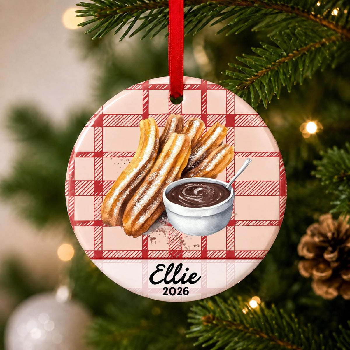 Close-up of the personalized churro ceramic ornament with name and year on red plaid hanging on a Christmas tree