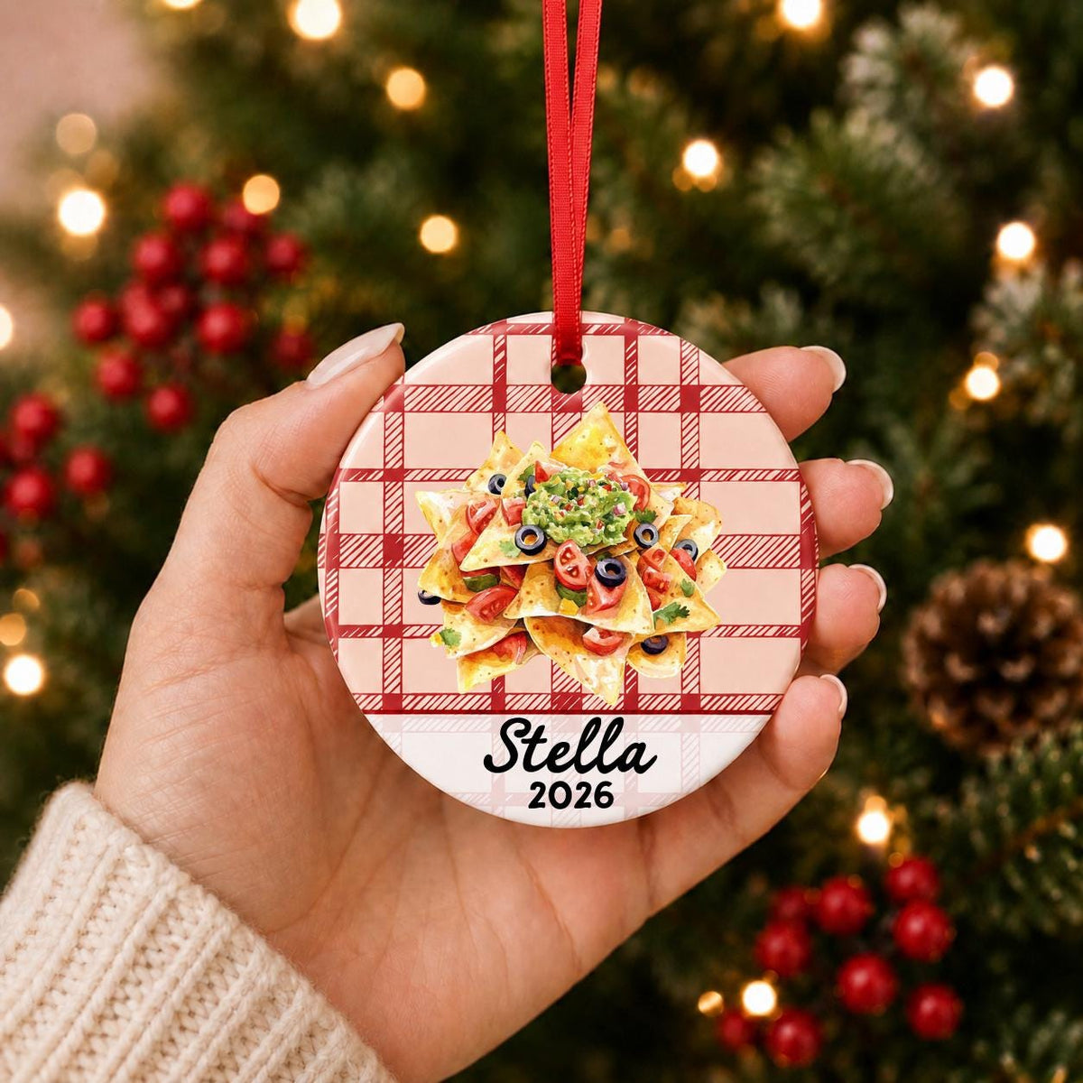 Hand holding the personalized nachos ceramic ornament with name and year on red plaid in front of a Christmas tree