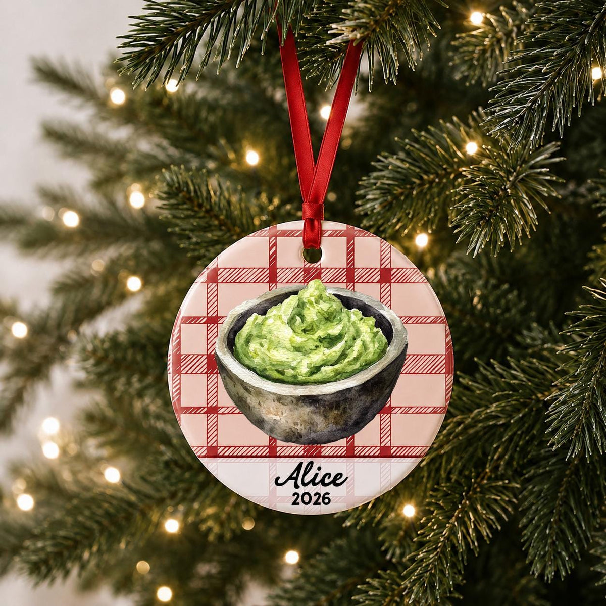 Personalized guacamole ceramic ornament with name and year on red plaid hanging on a lit Christmas tree