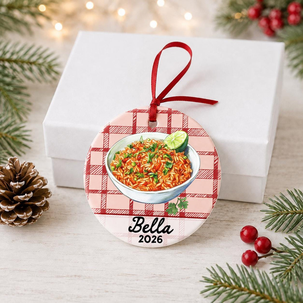 Personalized Mexican rice ceramic ornament with name and year on red plaid in front of a white gift box with pinecones and red berries