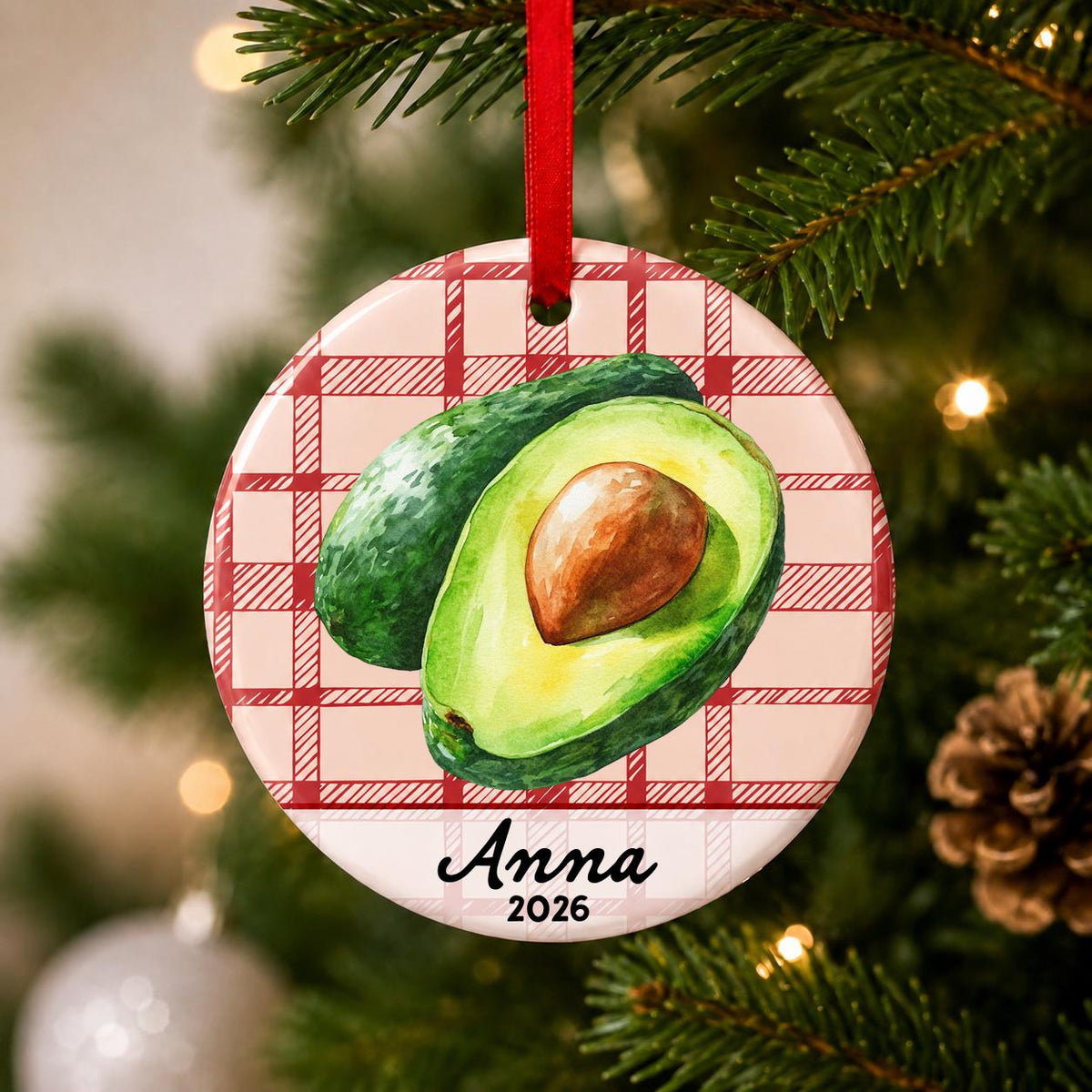 Close-up of the personalized avocado ceramic ornament with name and year on red plaid hanging on a Christmas tree