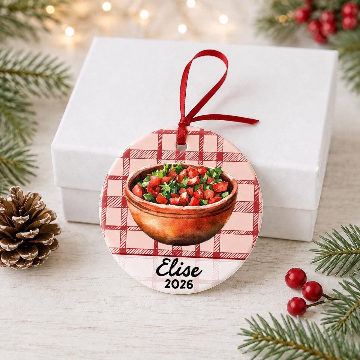 Personalized pico de gallo ceramic ornament with name and year on red plaid in front of a white gift box with pinecones and red berries