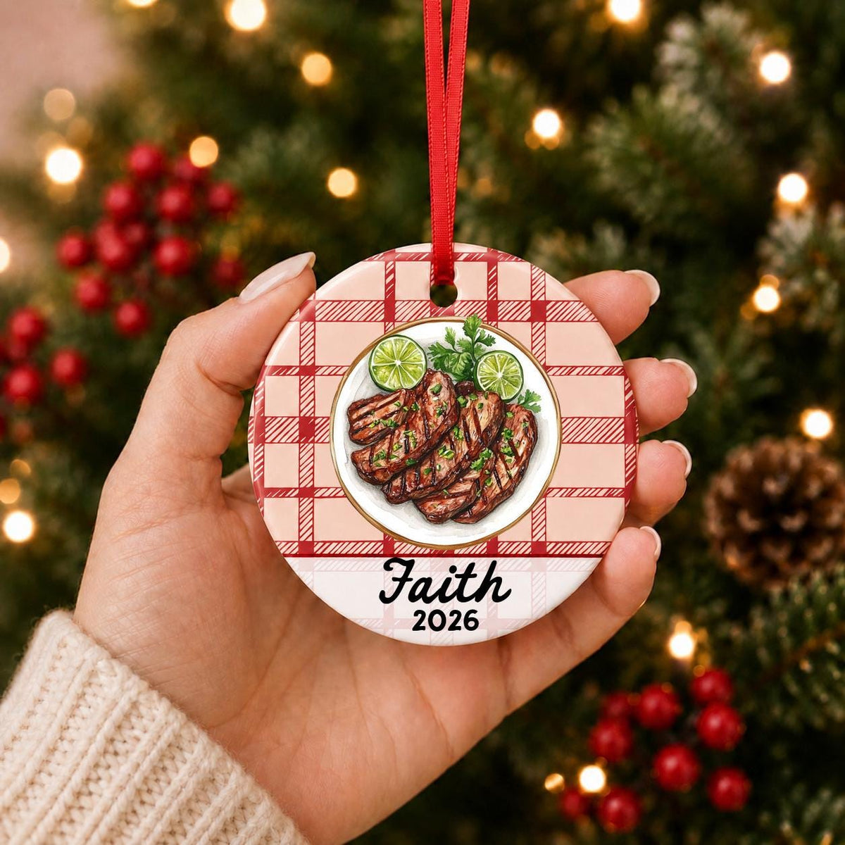 Hand holding the personalized carne asada ceramic ornament with name and year on red plaid in front of a Christmas tree