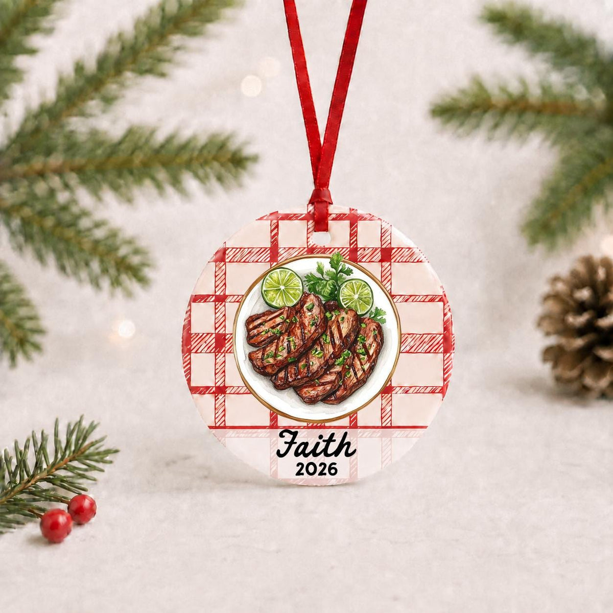 Personalized carne asada ceramic ornament with name and year on red plaid with red ribbon on a white surface with pine branches and pinecones