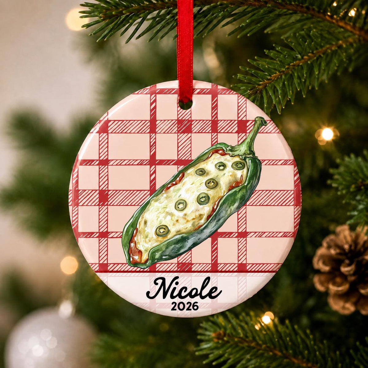 Close-up of the personalized chile relleno ceramic ornament with name and year on red plaid hanging on a Christmas tree