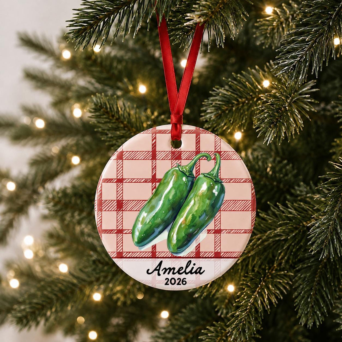 Personalized jalapeño ceramic ornament with name and year on red plaid hanging on a lit Christmas tree