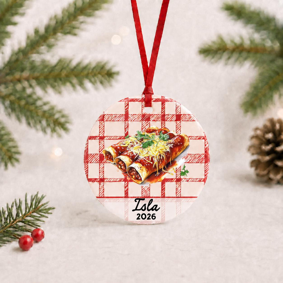 Personalized enchilada ceramic ornament with name and year on red plaid with red ribbon on a white surface with pine branches and pinecones
