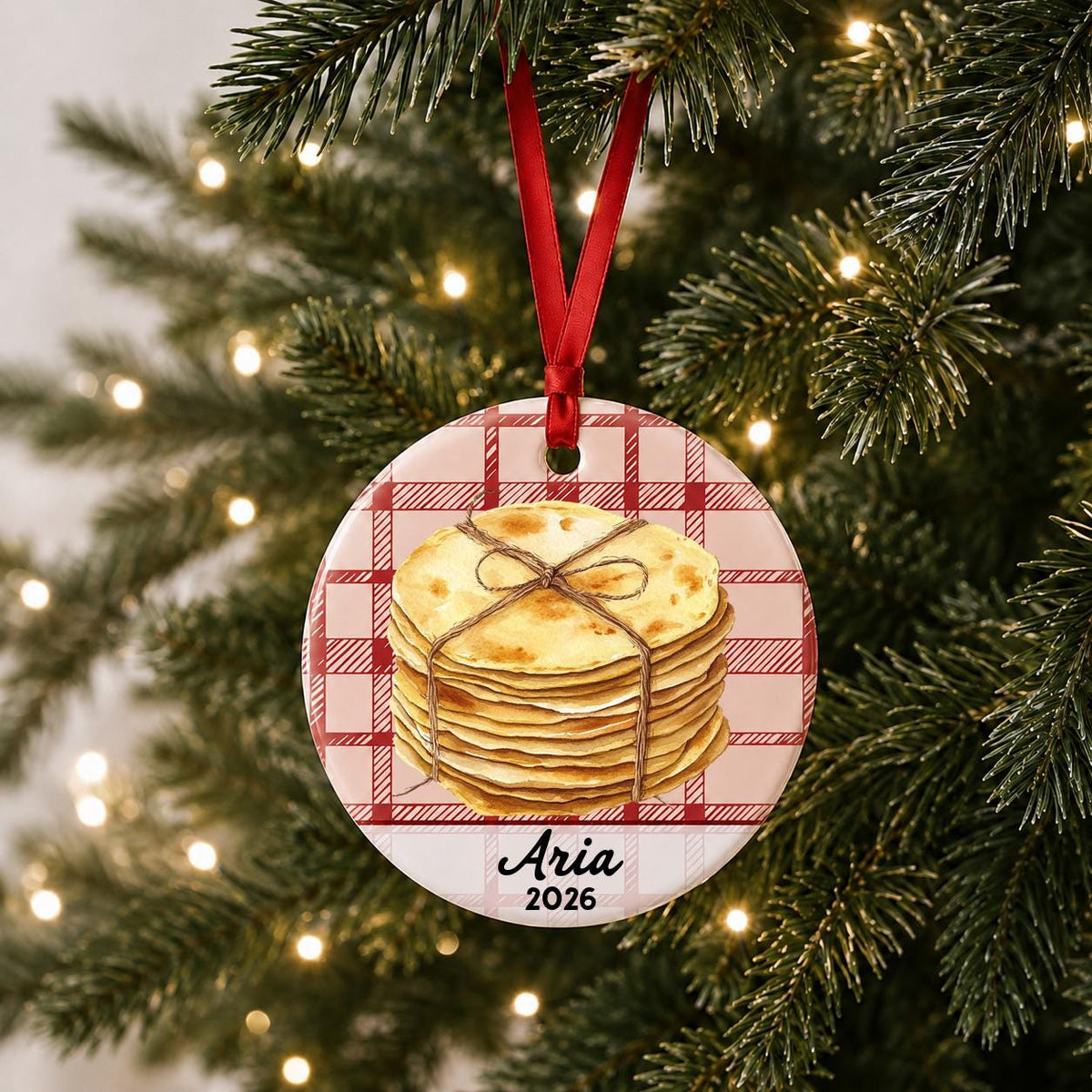 Personalized tortilla ceramic ornament with name and year on red plaid hanging on a lit Christmas tree