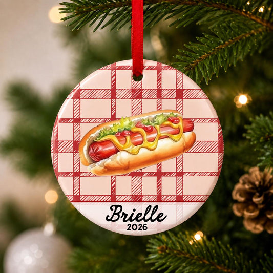 Close-up of the personalized hot dog ceramic ornament with name and year on red plaid hanging on a Christmas tree