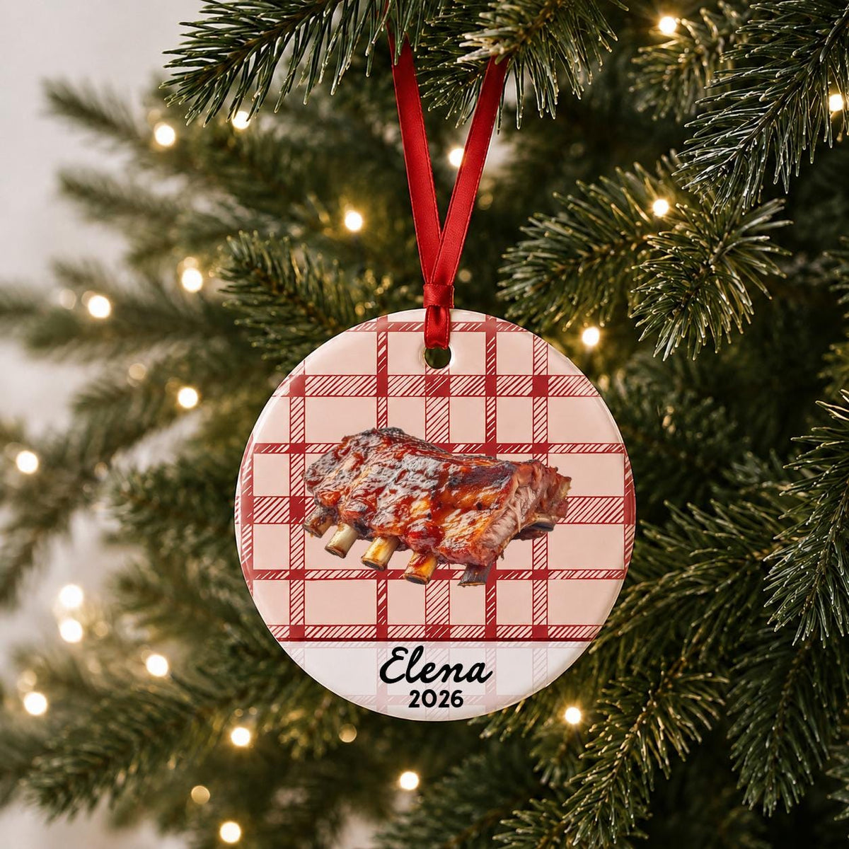 Personalized BBQ ribs ceramic ornament with name and year on red plaid hanging on a lit Christmas tree