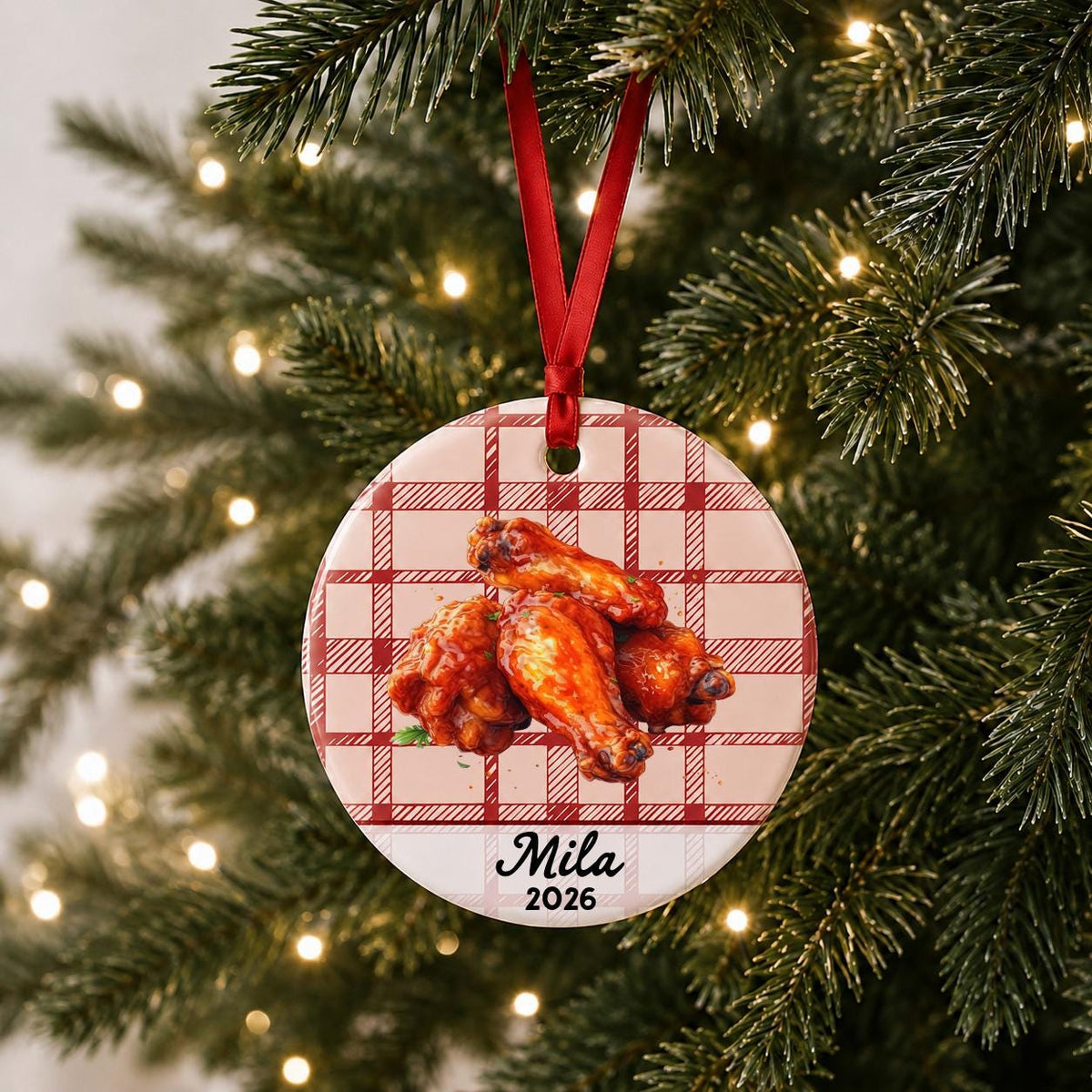 Personalized buffalo wings ceramic ornament with name and year on red plaid hanging on a lit Christmas tree