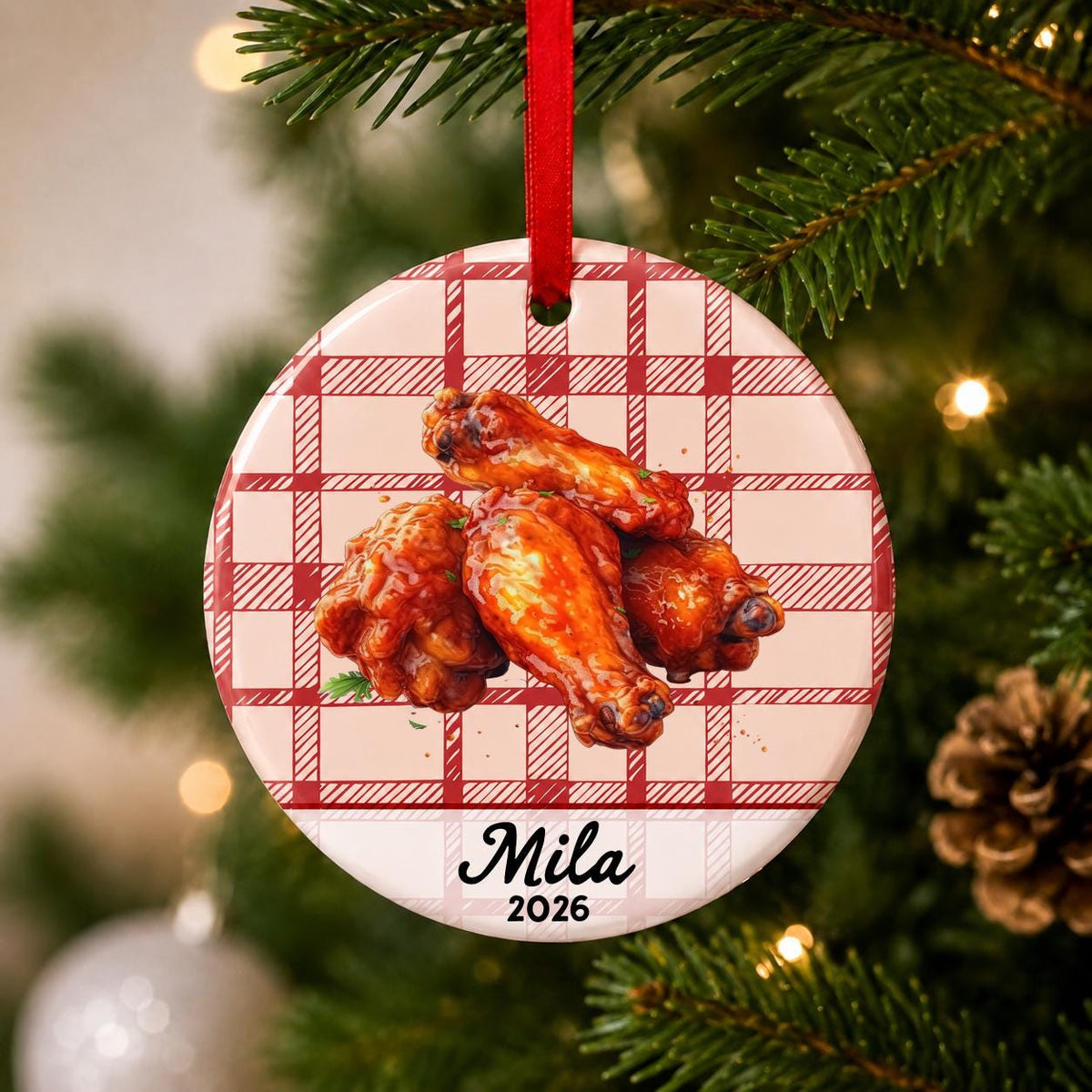 Close-up of the personalized buffalo wings ceramic ornament with name and year on red plaid hanging on a Christmas tree