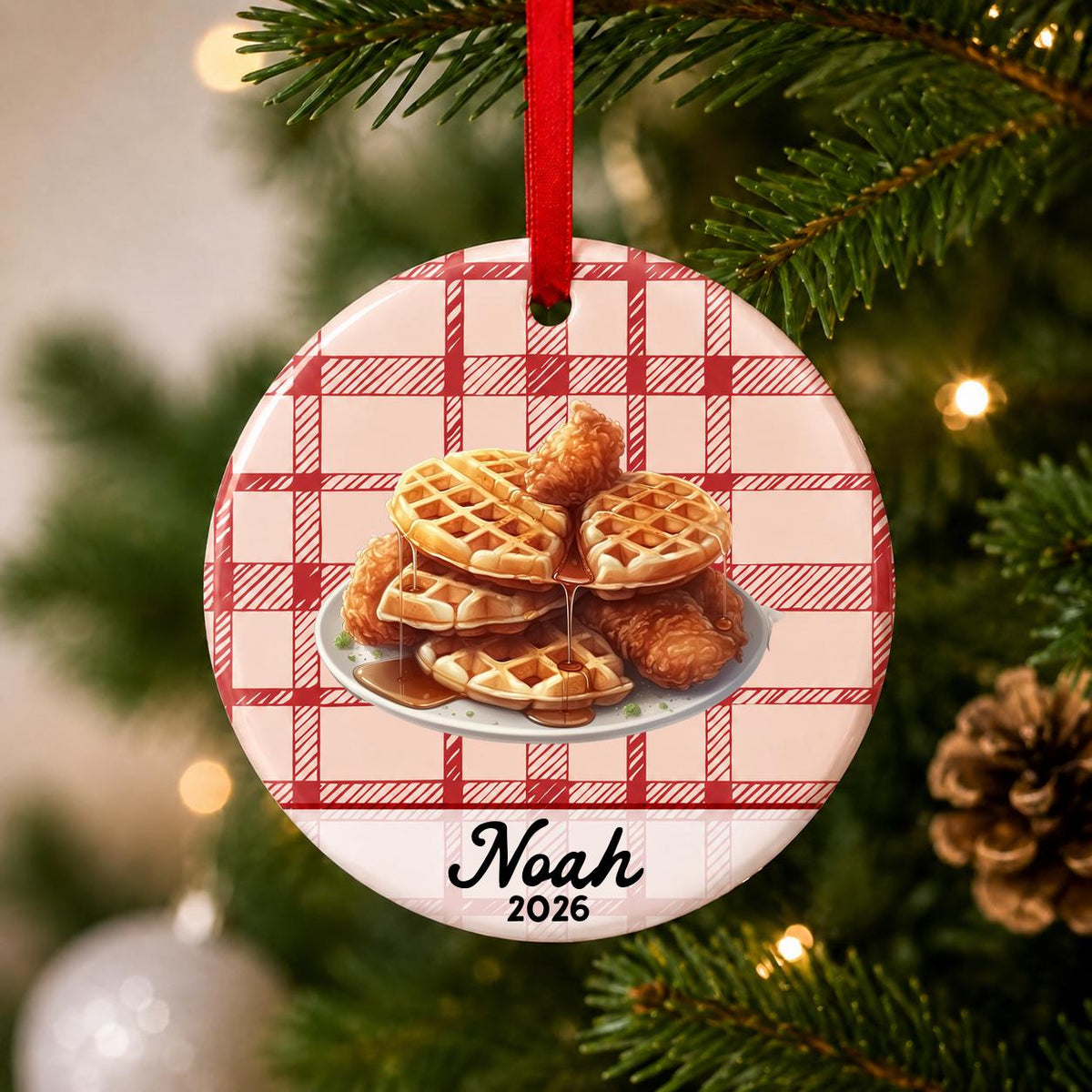 Close-up of the personalized chicken and waffles ceramic ornament with name and year on red plaid hanging on a Christmas tree