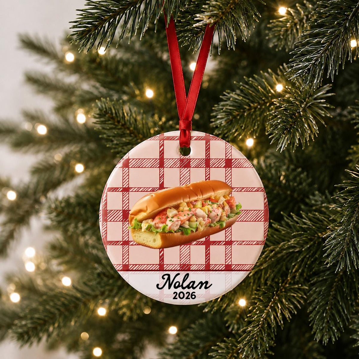 Personalized lobster roll ceramic ornament with name and year on red plaid hanging on a lit Christmas tree