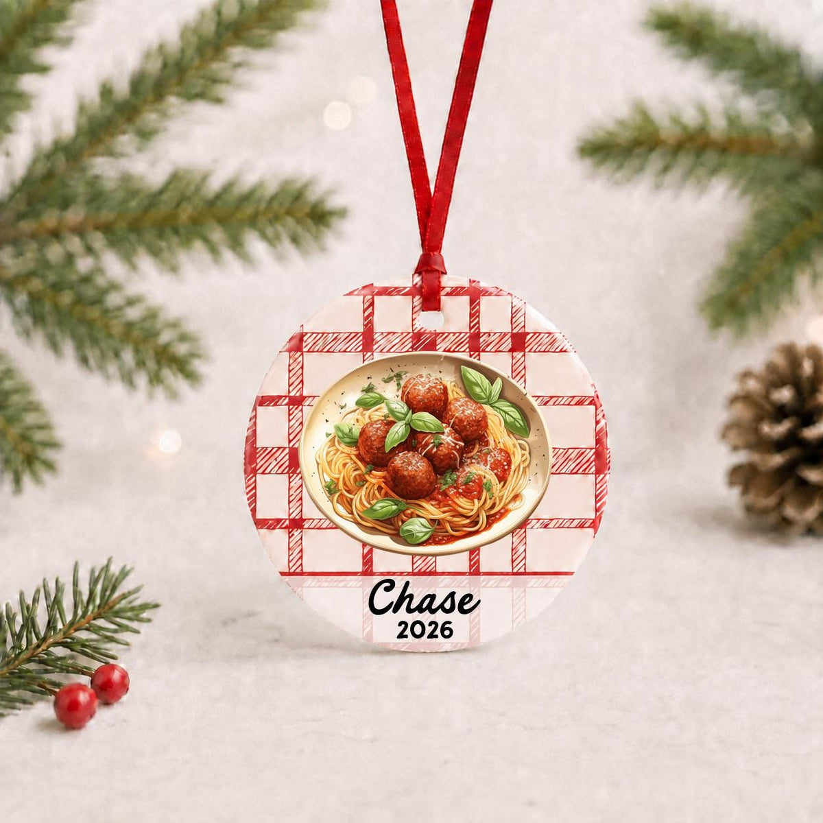 Personalized spaghetti and meatballs ceramic ornament with name and year on red plaid with red ribbon on a white surface with pine branches and pinecones