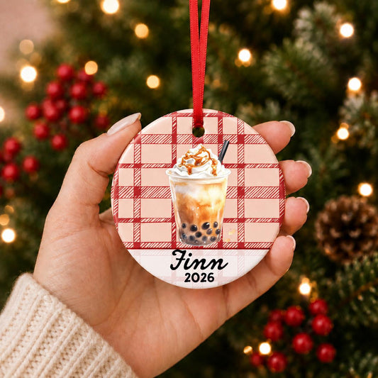 Hand holding the personalized brown sugar boba ceramic ornament with name and year on red plaid in front of a Christmas tree