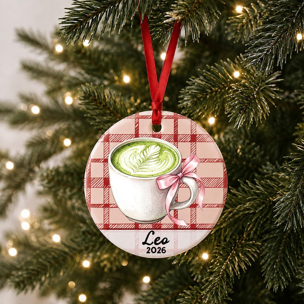 Personalized matcha latte ceramic ornament with name and year on red plaid hanging on a lit Christmas tree