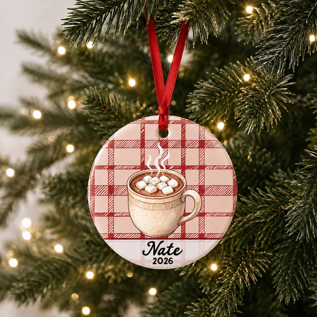 Personalized hot chocolate ceramic ornament with name and year on red plaid hanging on a lit Christmas tree