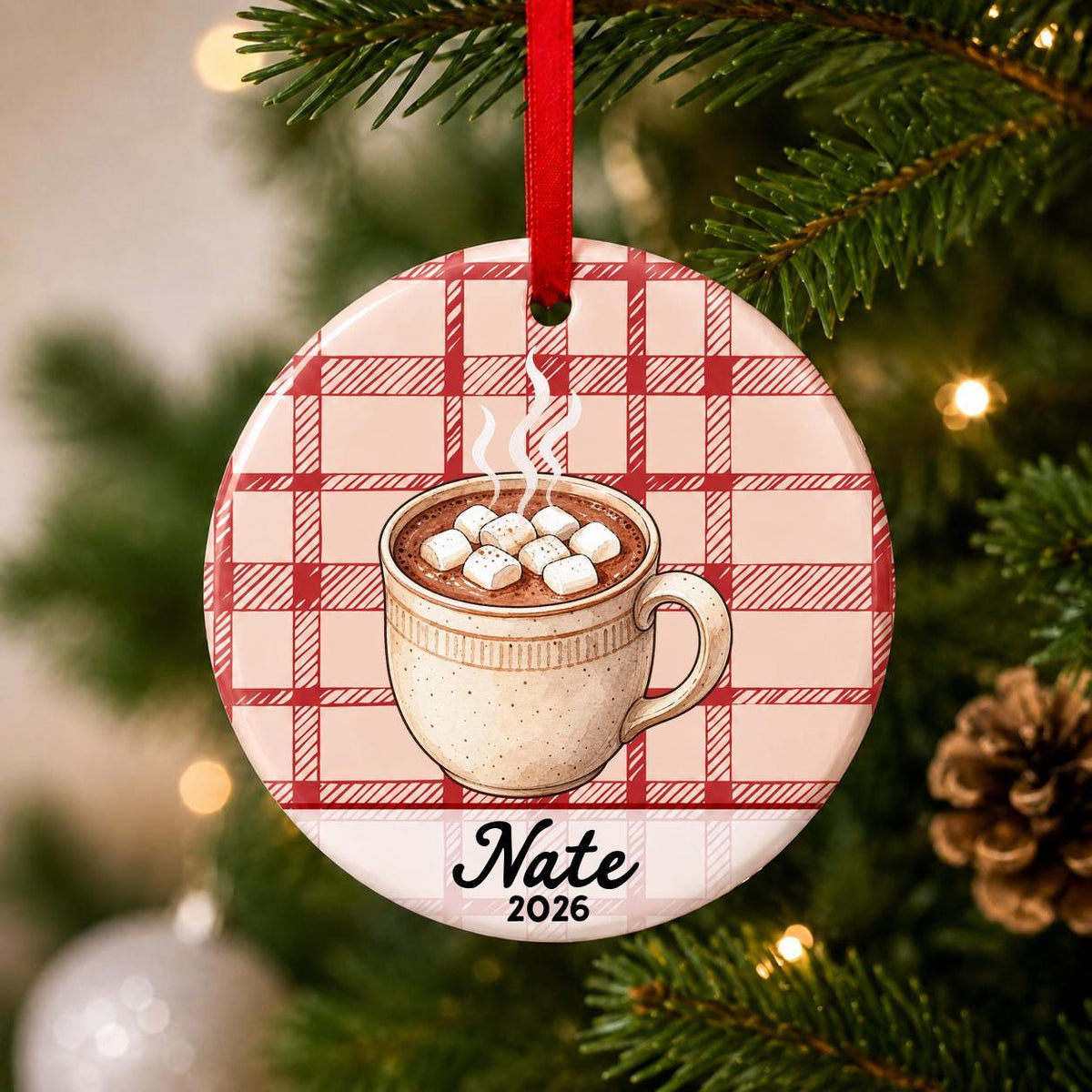 Close-up of the personalized hot chocolate ceramic ornament with name and year on red plaid hanging on a Christmas tree