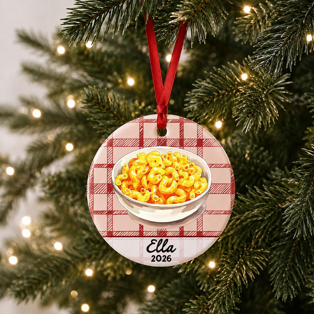 Personalized mac and cheese ceramic ornament with name and year on red plaid hanging on a lit Christmas tree