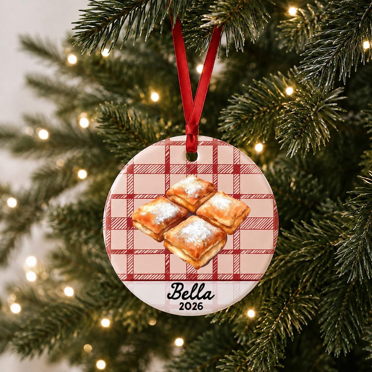 Personalized beignets ceramic ornament with name and year on red plaid hanging on a lit Christmas tree