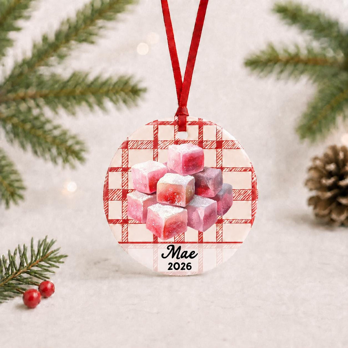 Personalized turkish delight ceramic ornament with name and year on red plaid with red ribbon on a white surface with pine branches and pinecones