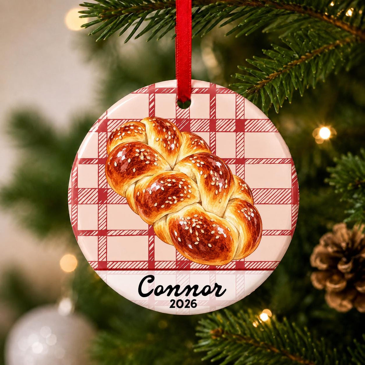 Close-up of the personalized challah bread ceramic ornament with name and year on red plaid hanging on a Christmas tree