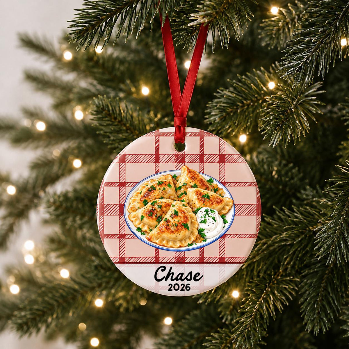 Personalized pierogi ceramic ornament with name and year on red plaid hanging on a lit Christmas tree