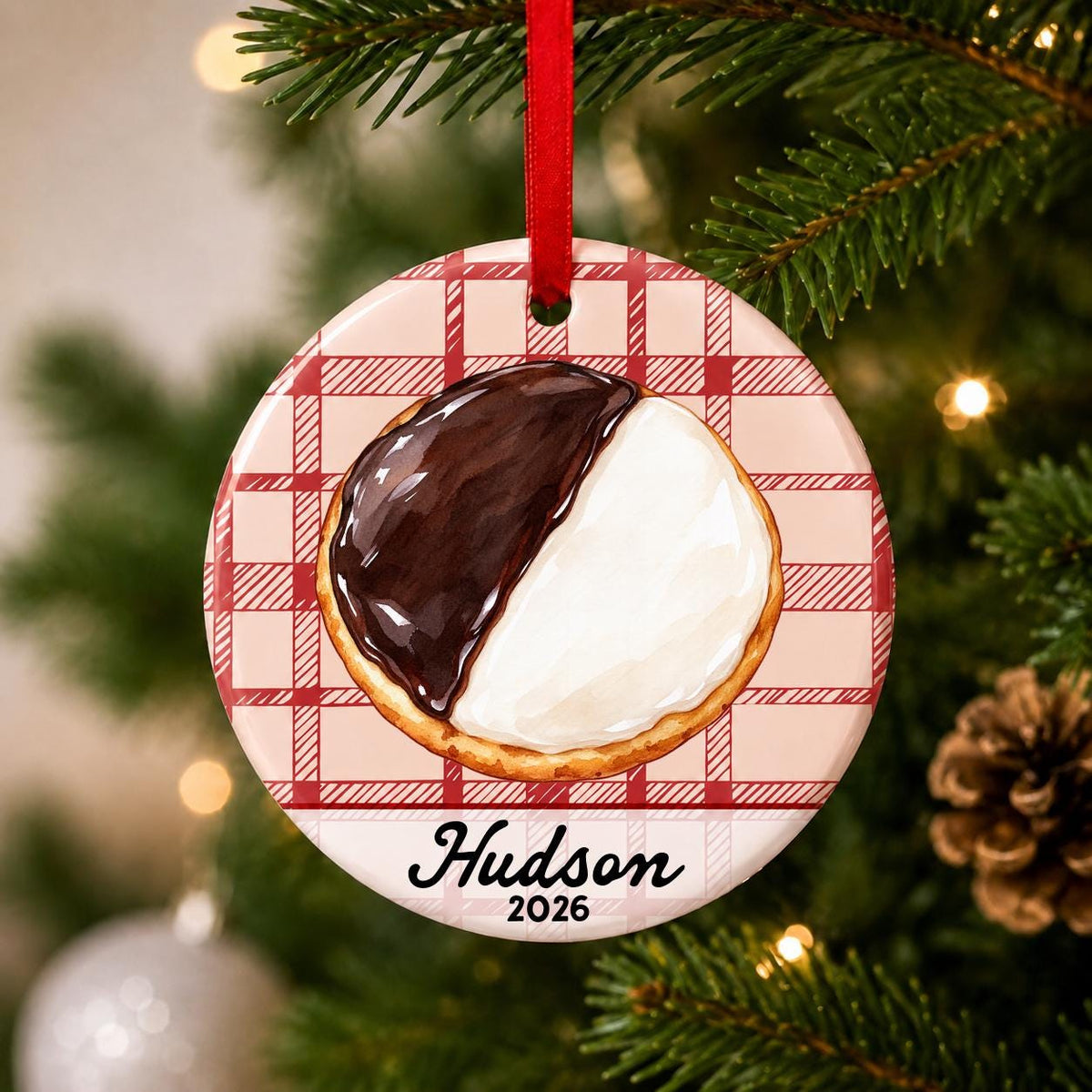 Close-up of the personalized black and white cookie ceramic ornament with name and year on red plaid hanging on a Christmas tree