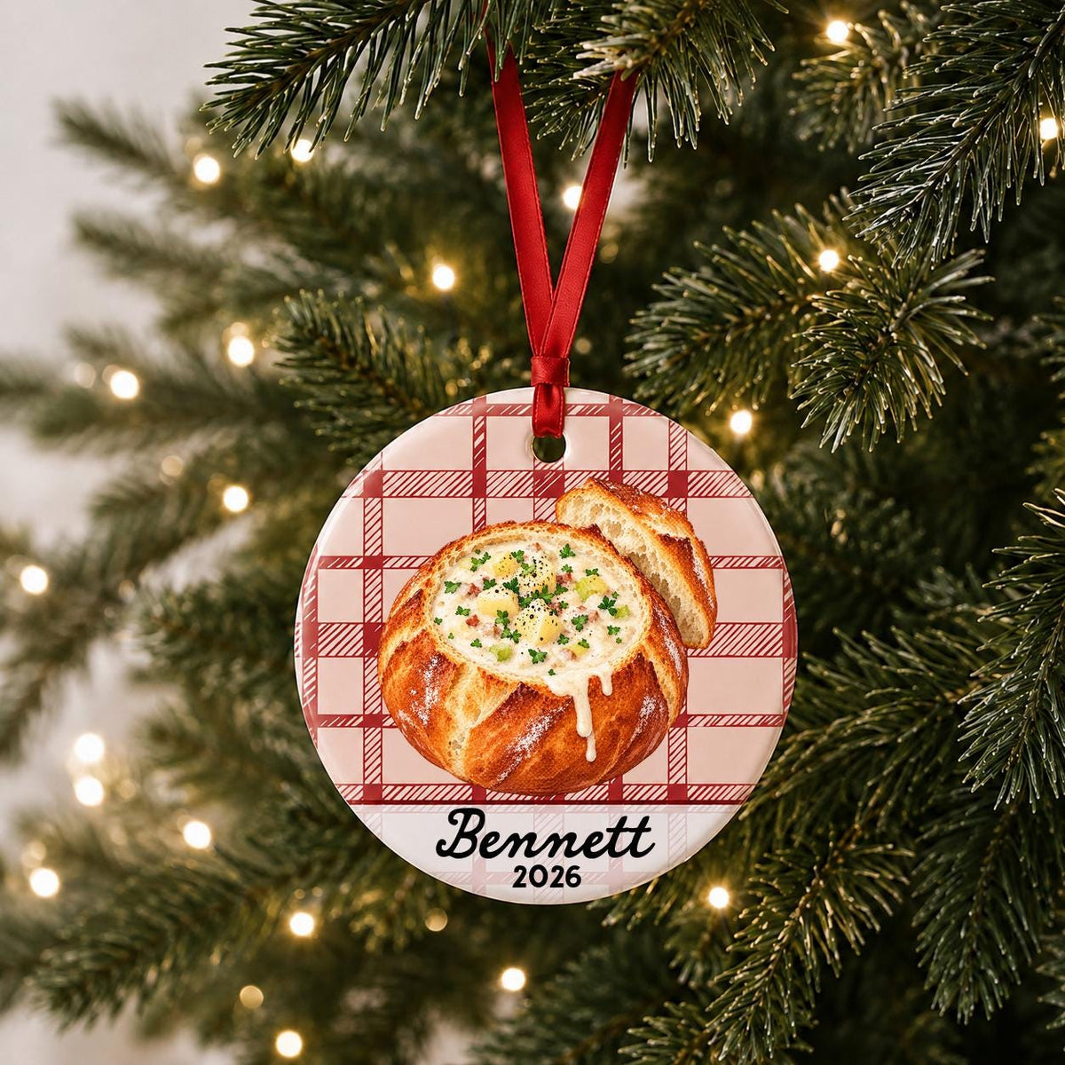 Personalized clam chowder bread bowl ceramic ornament with name and year on red plaid hanging on a lit Christmas tree