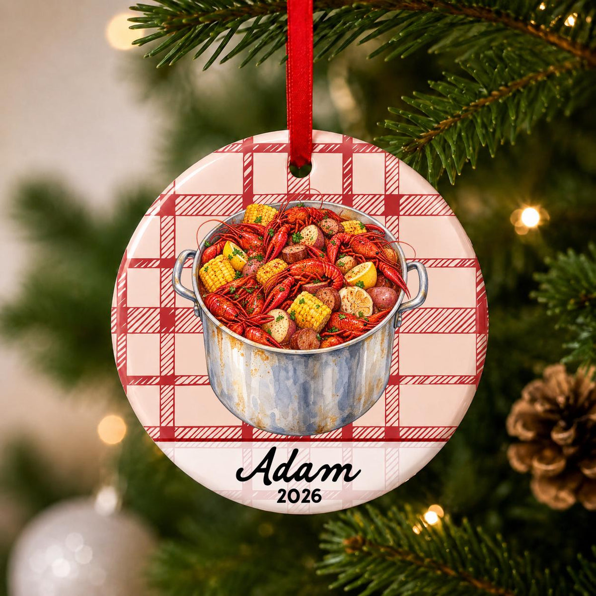 Close-up of the personalized crawfish boil ceramic ornament with name and year on red plaid hanging on a Christmas tree