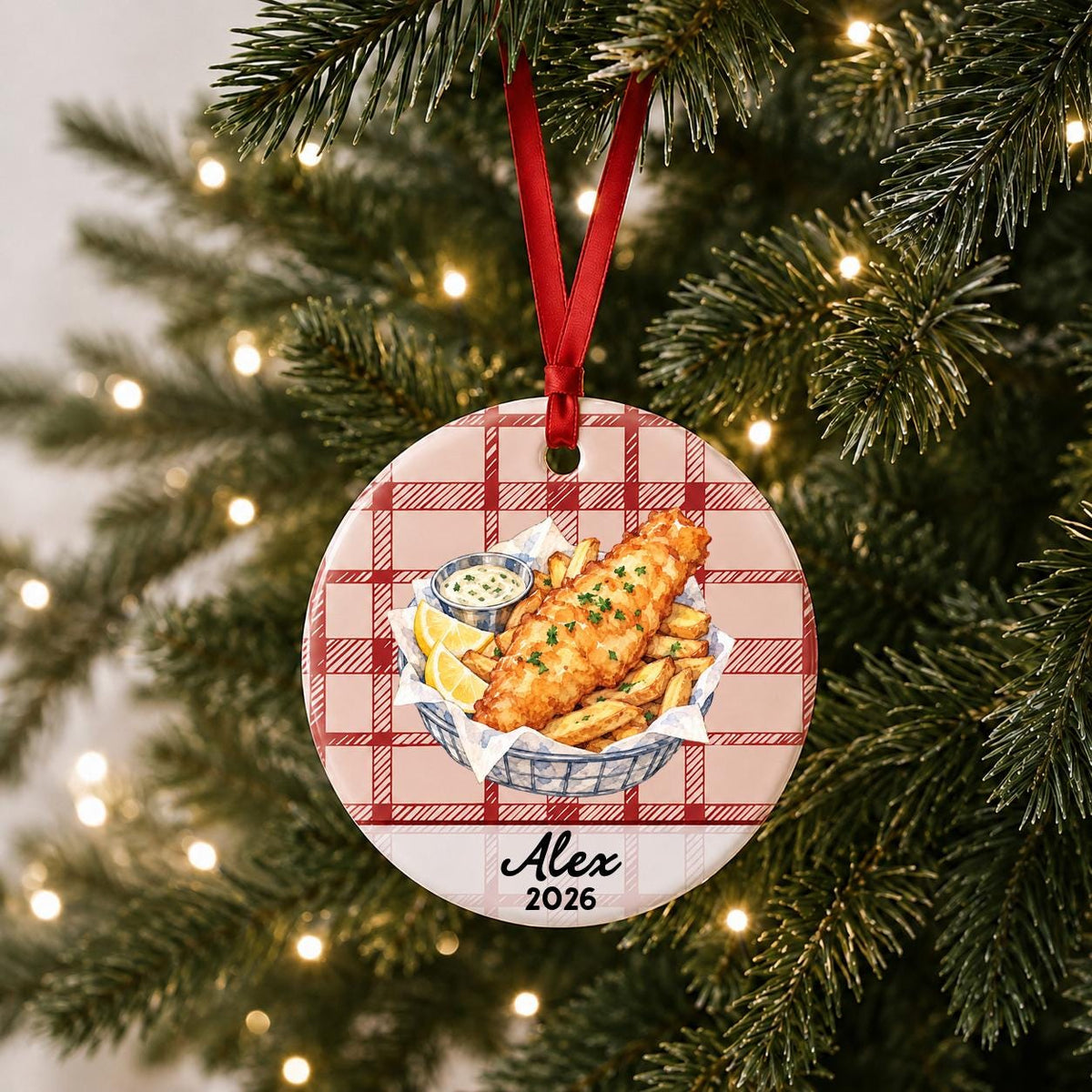Personalized fish and chips ceramic ornament with name and year on red plaid hanging on a lit Christmas tree