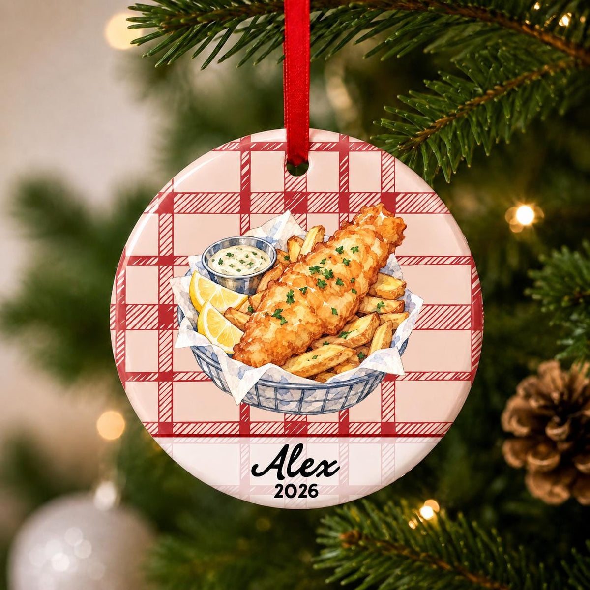 Close-up of the personalized fish and chips ceramic ornament with name and year on red plaid hanging on a Christmas tree