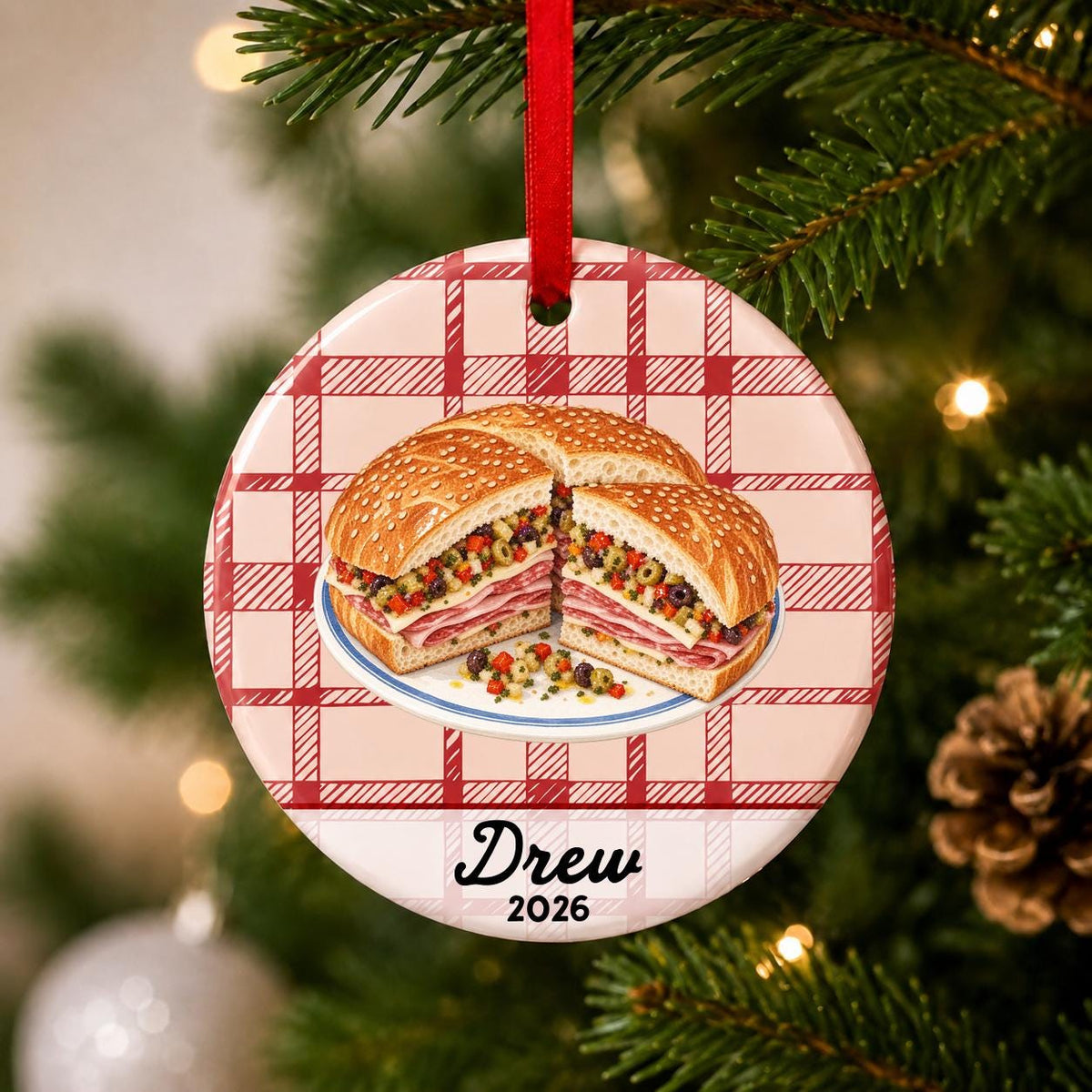 Close-up of the personalized muffuletta ceramic ornament with name and year on red plaid hanging on a Christmas tree