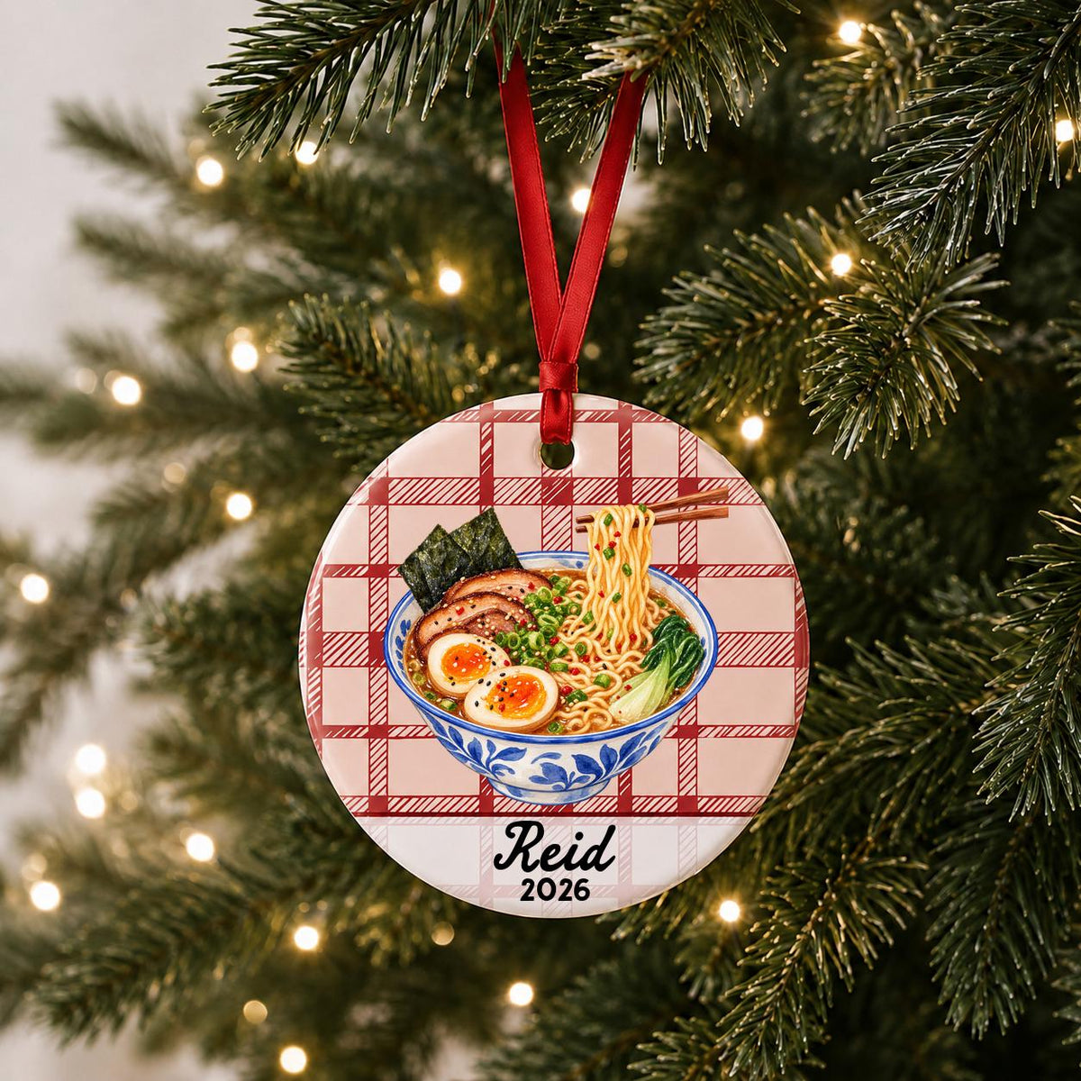 Personalized ramen ceramic ornament with name and year on red plaid hanging on a lit Christmas tree