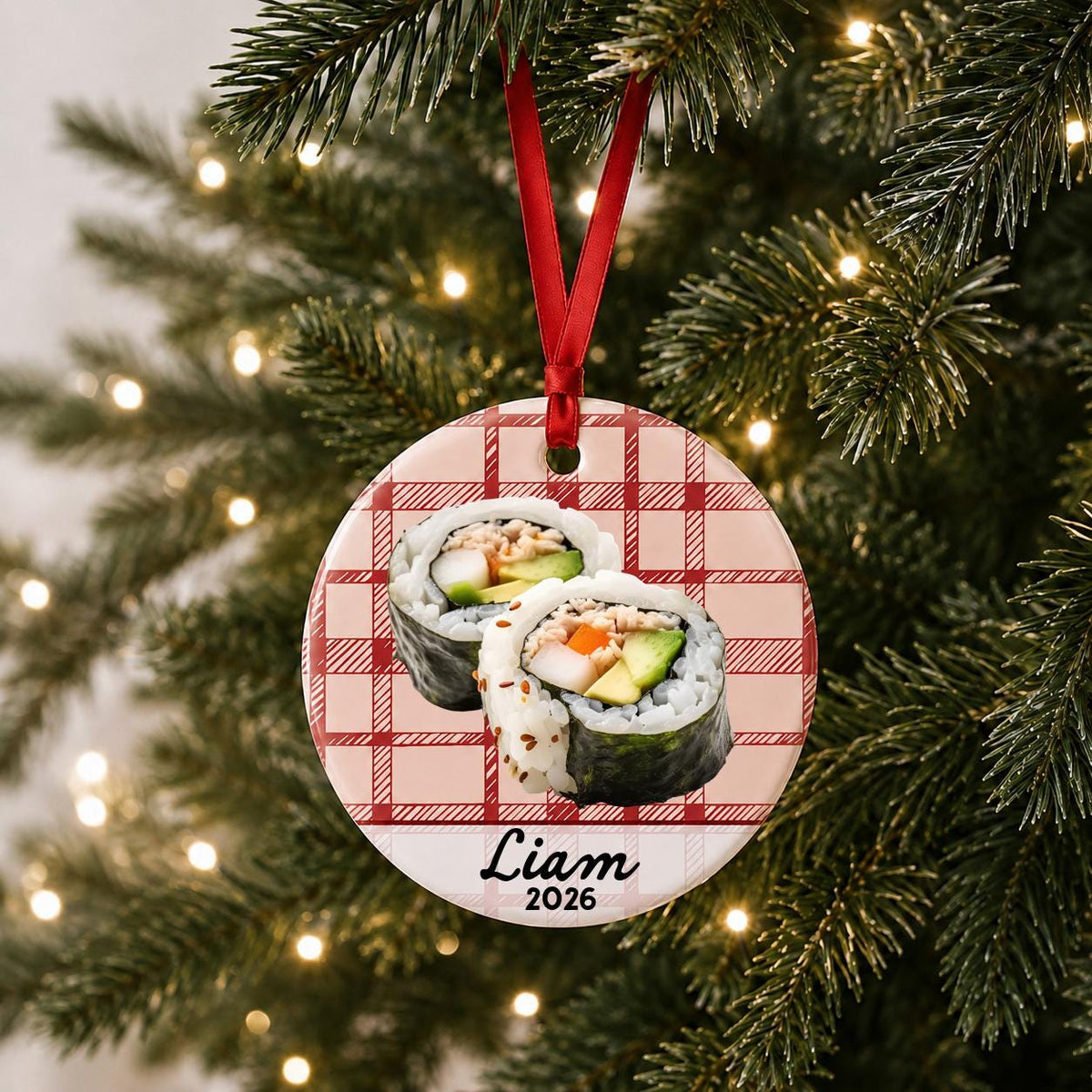 Personalized sushi ceramic ornament with name and year on red plaid hanging on a lit Christmas tree