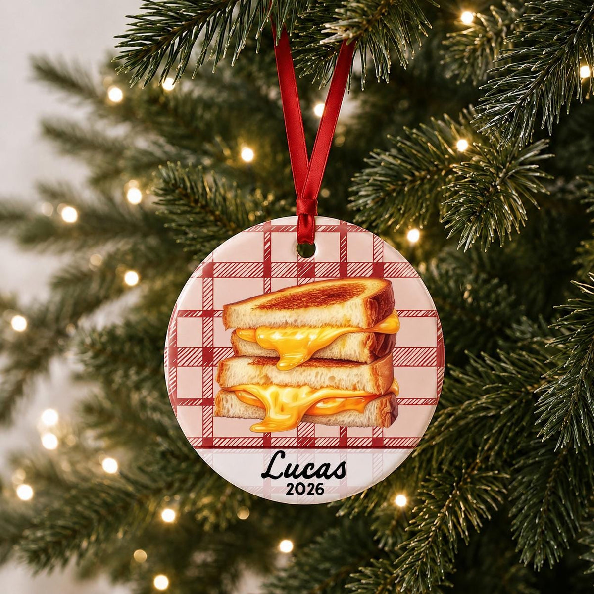 Personalized grilled cheese ceramic ornament with name and year on red plaid hanging on a lit Christmas tree
