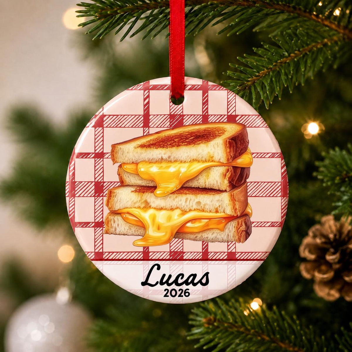 Close-up of the personalized grilled cheese ceramic ornament with name and year on red plaid hanging on a Christmas tree