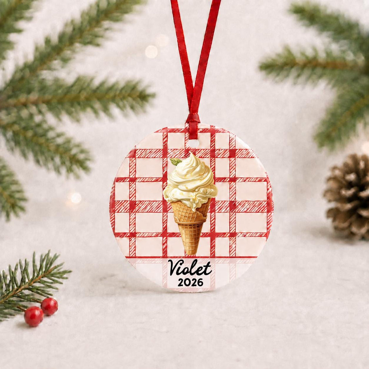 Personalized soft serve ice cream ceramic ornament with name and year on red plaid with red ribbon on a white surface with pine branches and pinecones