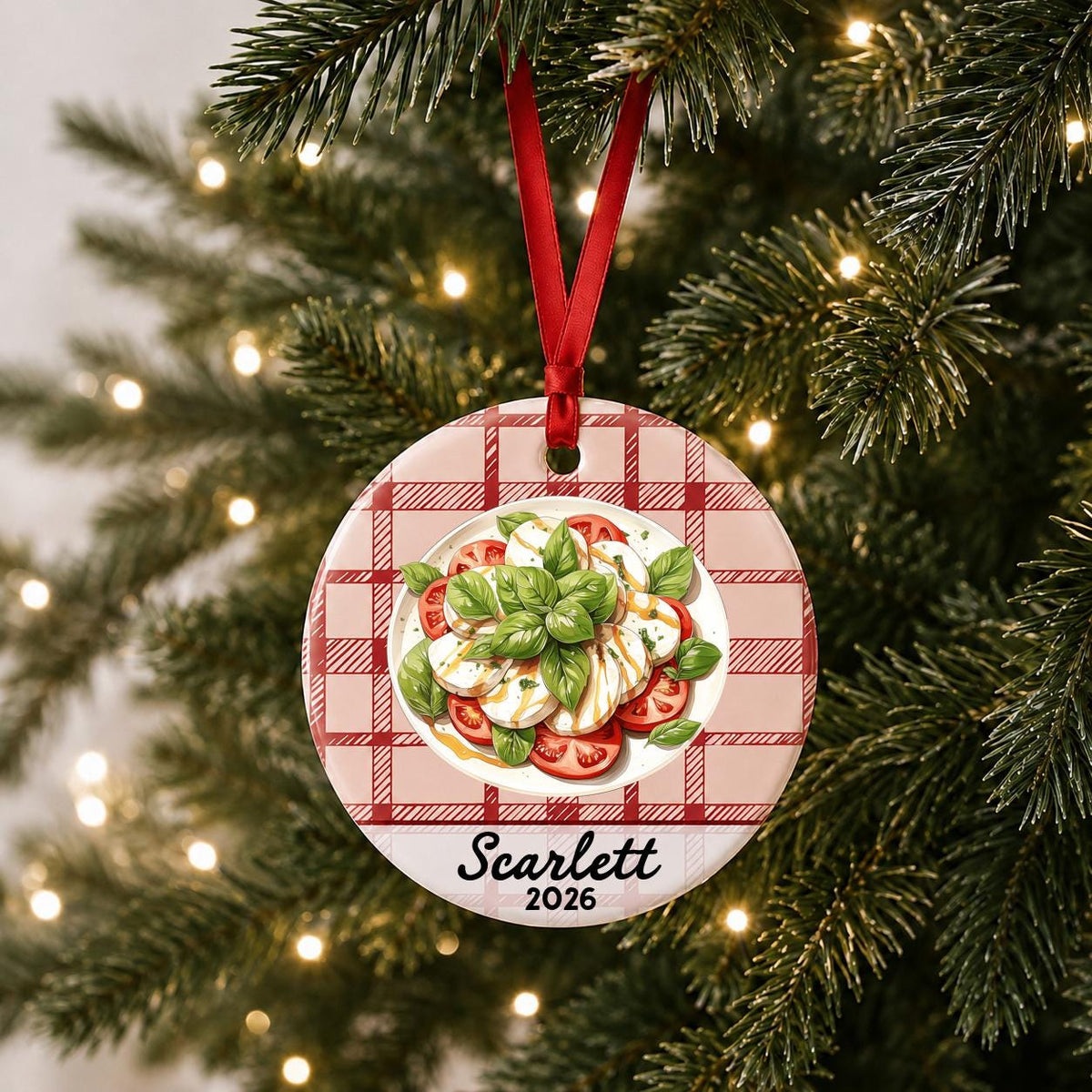 Personalized caprese salad ceramic ornament with name and year on red plaid hanging on a lit Christmas tree