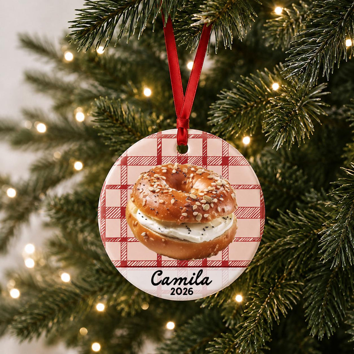 Personalized bagel ceramic ornament with name and year on red plaid hanging on a lit Christmas tree