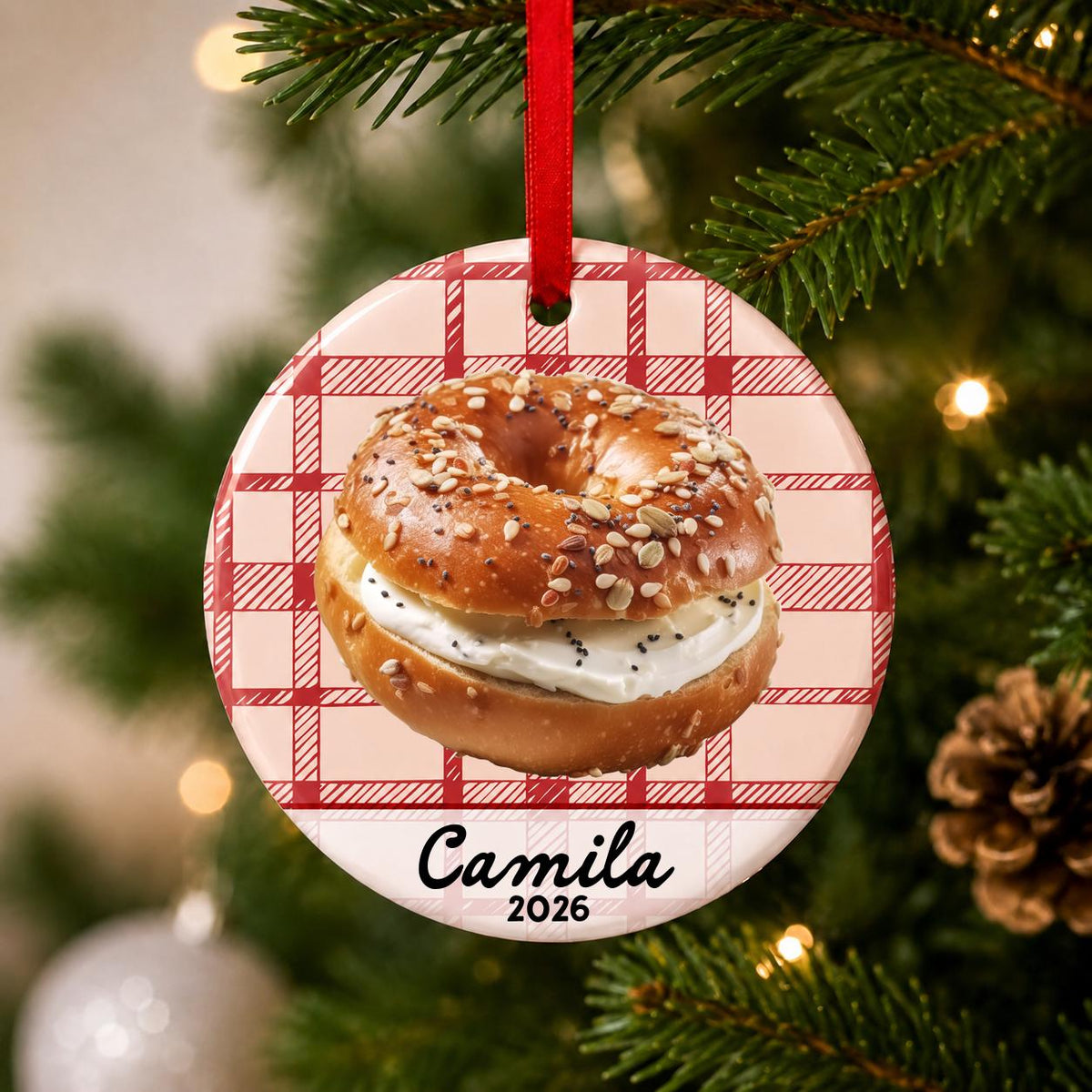 Close-up of the personalized bagel ceramic ornament with name and year on red plaid hanging on a Christmas tree