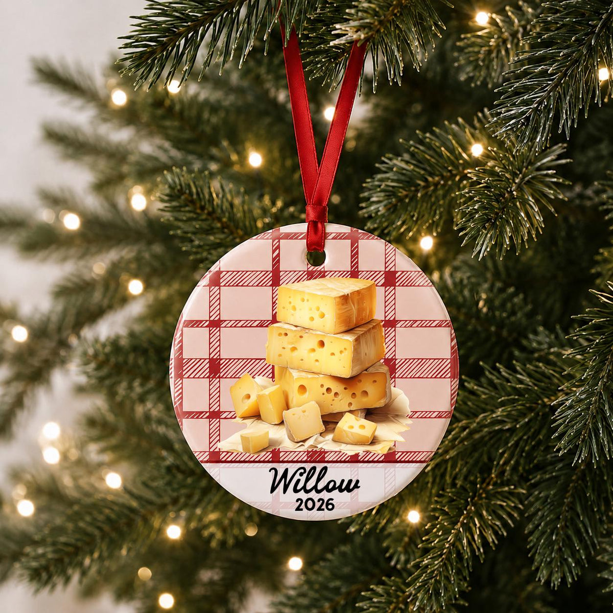 Personalized Swiss cheese ceramic ornament with name and year on red plaid hanging on a lit Christmas tree