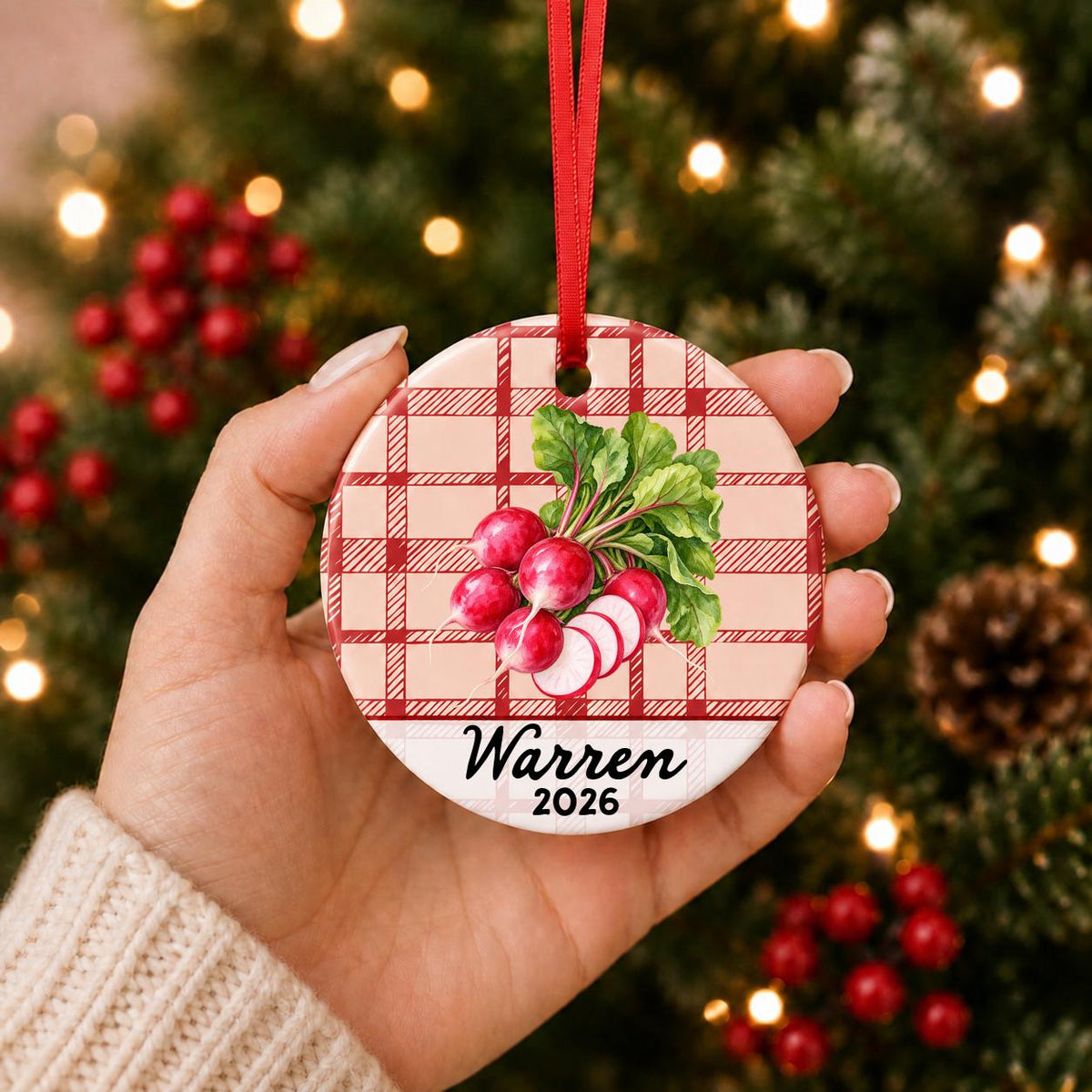 Hand holding the personalized radishes ceramic ornament with name and year on red plaid in front of a Christmas tree