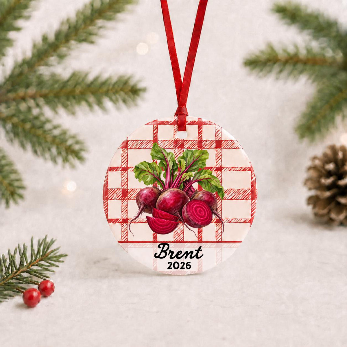 Personalized beets ceramic ornament with name and year on red plaid with red ribbon on a white surface with pine branches and pinecones